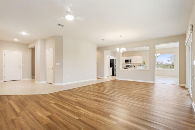 unfurnished living room featuring visible vents, light wood-style flooring, ceiling fan with notable chandelier, and baseboards