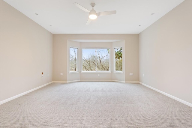 spare room featuring light colored carpet, baseboards, and ceiling fan