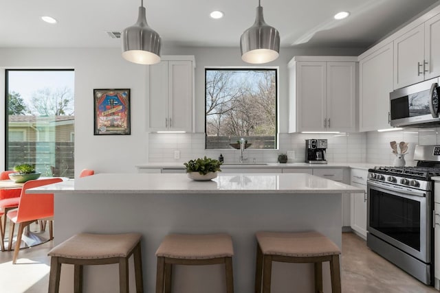 kitchen with a sink, a kitchen breakfast bar, plenty of natural light, appliances with stainless steel finishes, and decorative backsplash