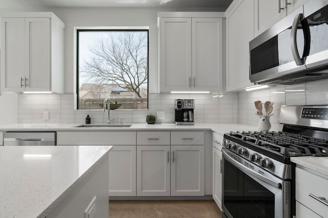 kitchen with a sink, light stone counters, appliances with stainless steel finishes, white cabinets, and decorative backsplash