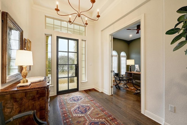 entrance foyer featuring dark wood finished floors, a notable chandelier, baseboards, and ornamental molding