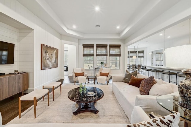 living room featuring wooden walls, wood finished floors, visible vents, recessed lighting, and a raised ceiling