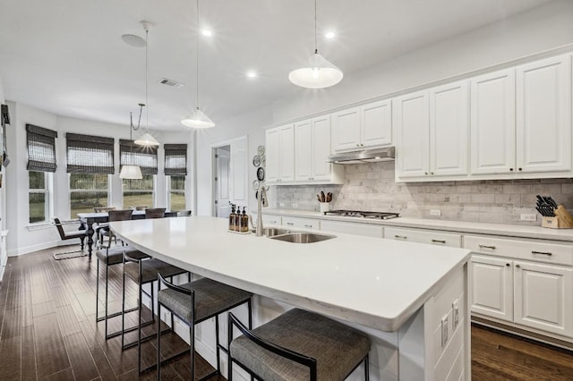 kitchen with under cabinet range hood, visible vents, backsplash, and dark wood-style flooring