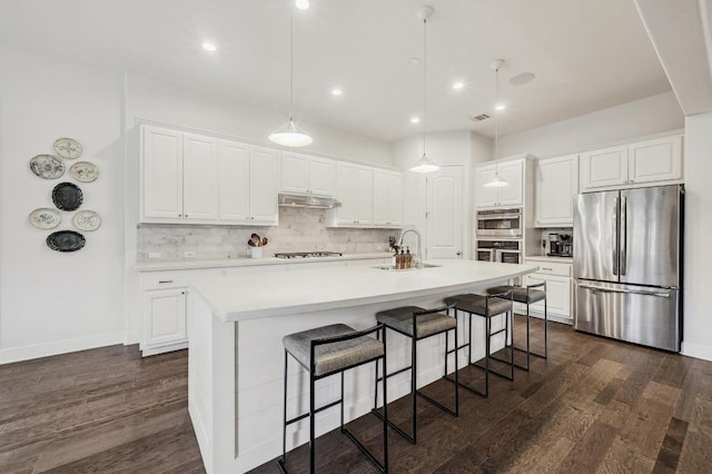 kitchen featuring backsplash, under cabinet range hood, dark wood finished floors, a kitchen bar, and appliances with stainless steel finishes