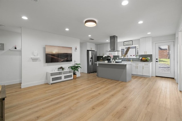 kitchen with light wood-style flooring, decorative backsplash, white cabinetry, stainless steel fridge, and island range hood