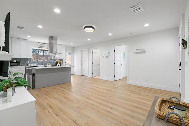 kitchen featuring visible vents, backsplash, island range hood, and light wood finished floors