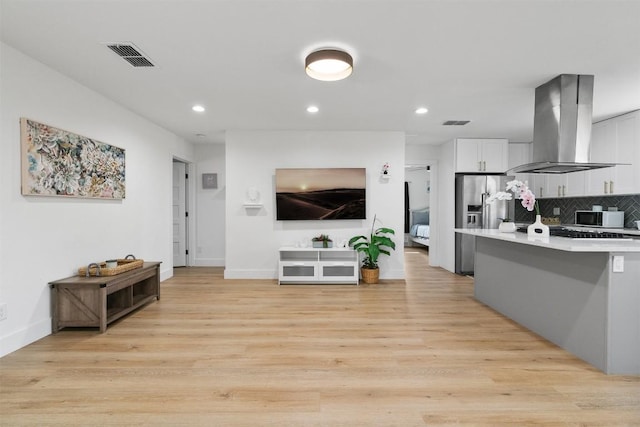 kitchen featuring white microwave, visible vents, stainless steel fridge with ice dispenser, light countertops, and island range hood