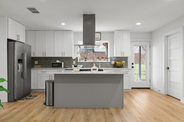 kitchen with visible vents, a kitchen island, island exhaust hood, light countertops, and appliances with stainless steel finishes