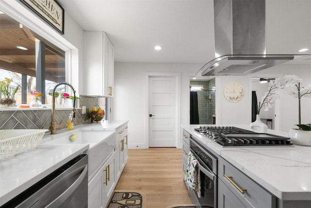 kitchen with range hood, white cabinets, appliances with stainless steel finishes, light wood-type flooring, and backsplash