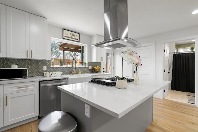 kitchen with light wood-type flooring, island exhaust hood, stainless steel appliances, white cabinets, and decorative backsplash