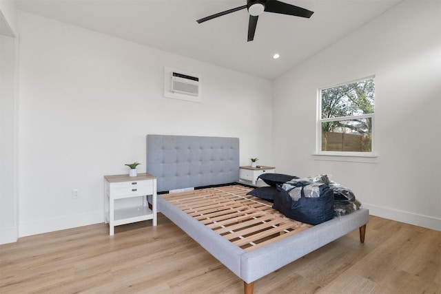 bedroom with lofted ceiling, a wall unit AC, recessed lighting, light wood-style floors, and baseboards