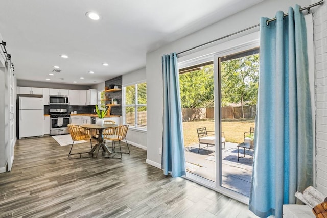 dining room featuring wood finished floors, baseboards, visible vents, recessed lighting, and a barn door