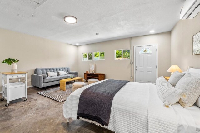 bedroom featuring finished concrete flooring, baseboards, attic access, a wall unit AC, and a textured ceiling