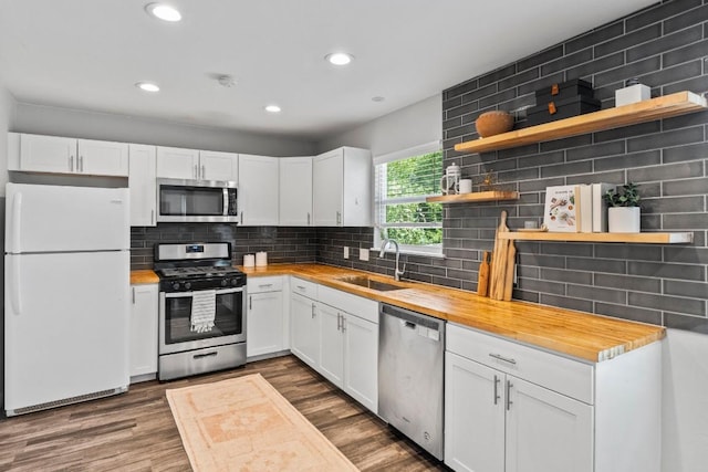 kitchen featuring open shelves, a sink, appliances with stainless steel finishes, wooden counters, and dark wood-style flooring