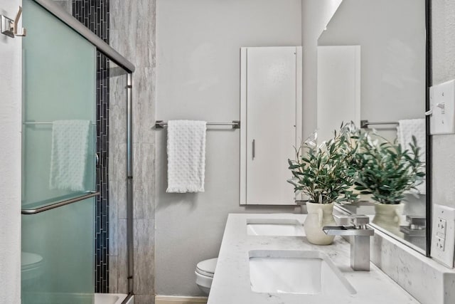 bathroom featuring baseboards, toilet, double vanity, an enclosed shower, and a sink