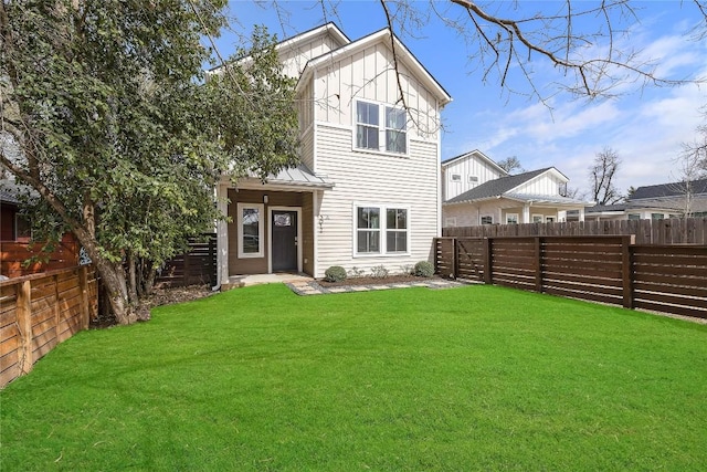 back of property with a fenced backyard, board and batten siding, and a yard