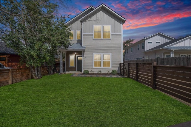 back of house at dusk with a lawn, board and batten siding, and a fenced backyard