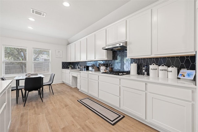 kitchen featuring tasteful backsplash, visible vents, under cabinet range hood, white cabinets, and gas stovetop