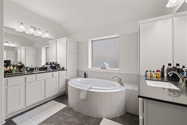 bathroom featuring vaulted ceiling, two vanities, a bath, and a sink