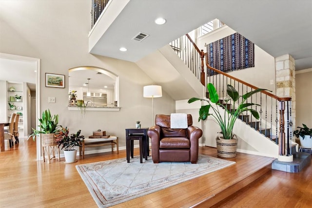 sitting room featuring visible vents, wood finished floors, baseboards, a towering ceiling, and stairs