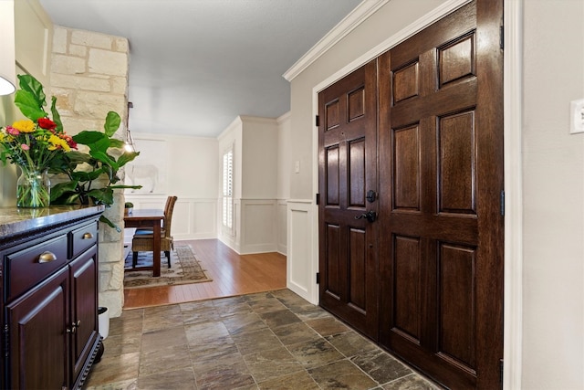 foyer entrance with stone finish flooring, crown molding, wainscoting, and a decorative wall