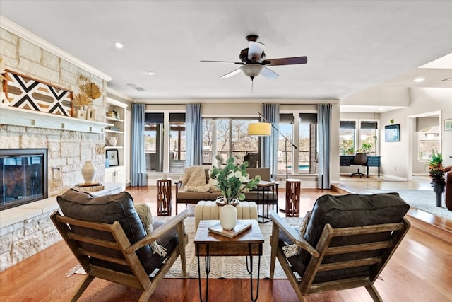 living room with a stone fireplace, crown molding, built in shelves, and wood finished floors