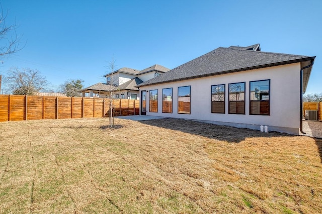 back of house featuring central air condition unit, a lawn, stucco siding, and fence