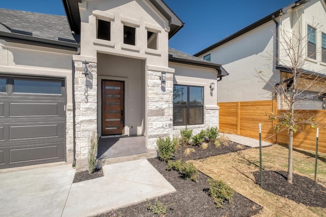 entrance to property featuring an attached garage, fence, stone siding, and stucco siding