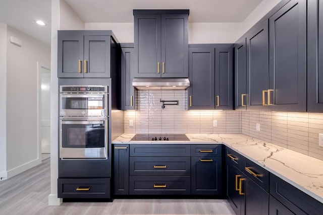 kitchen featuring under cabinet range hood, backsplash, stainless steel double oven, black electric cooktop, and light stone countertops