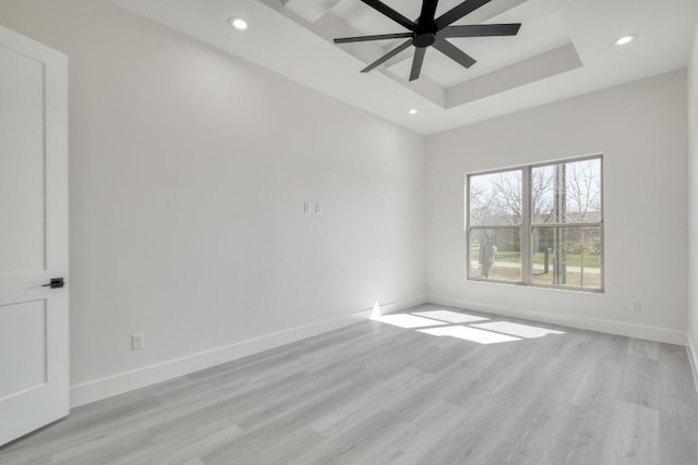 empty room with recessed lighting, baseboards, a raised ceiling, and light wood finished floors