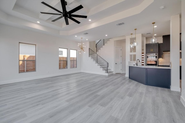 unfurnished living room featuring visible vents, baseboards, stairs, a tray ceiling, and a sink