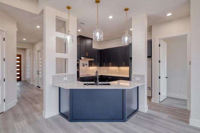 kitchen featuring light wood-type flooring, a sink, a peninsula, decorative backsplash, and light stone countertops