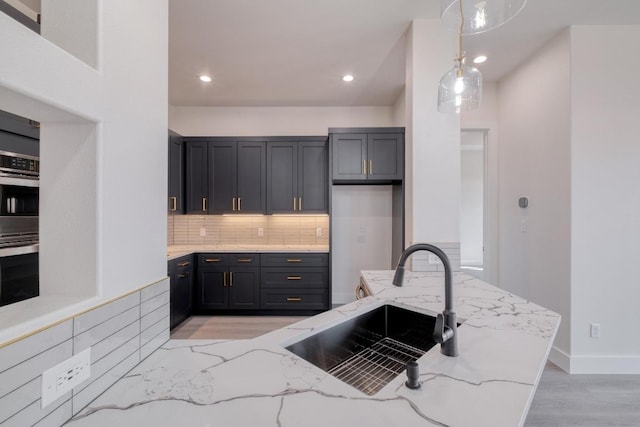 kitchen featuring backsplash, pendant lighting, light stone counters, recessed lighting, and a sink