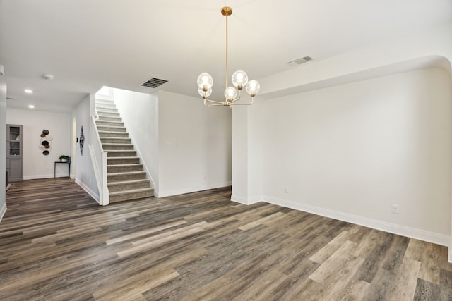 unfurnished room with visible vents, a notable chandelier, wood finished floors, and stairway