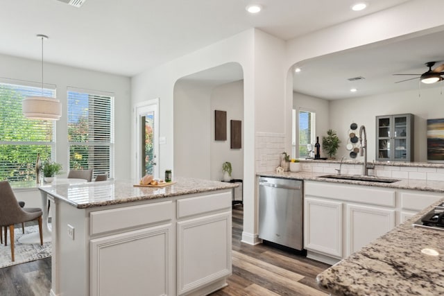 kitchen with dark wood finished floors, decorative backsplash, stainless steel dishwasher, white cabinets, and a sink