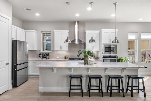 kitchen featuring visible vents, tasteful backsplash, appliances with stainless steel finishes, white cabinets, and wall chimney range hood