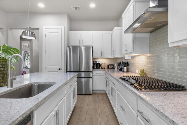 2505 Moreno St, Austin, TX 78723 - kitchen featuring appliances with stainless steel finishes, wall chimney exhaust hood, a sink, white cabinetry, and recessed lighting