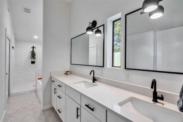 bathroom with a tile shower, visible vents, double vanity, and a sink