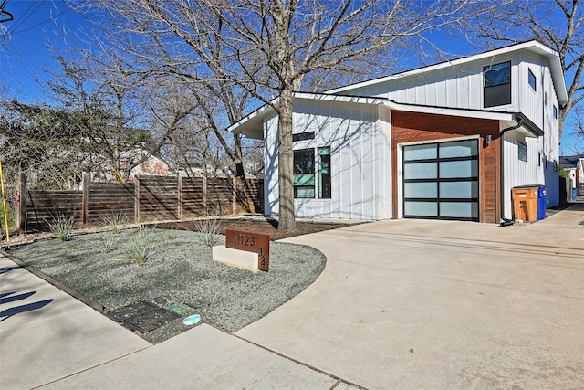 view of home's exterior with concrete driveway, board and batten siding, an attached garage, and fence