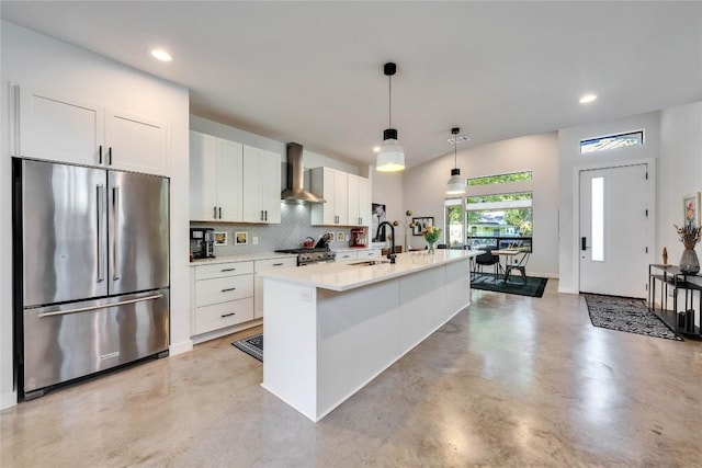 kitchen featuring wall chimney range hood, concrete flooring, white cabinets, stainless steel appliances, and a sink