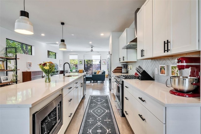 kitchen featuring high end stove, wall chimney range hood, open floor plan, decorative backsplash, and a sink