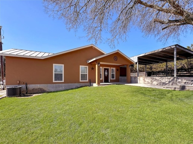 rear view of property featuring a standing seam roof, a yard, central AC unit, and stucco siding