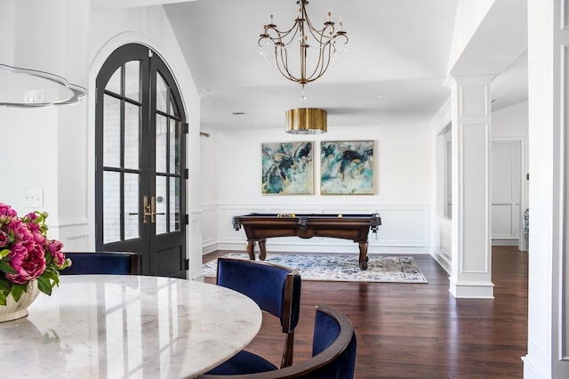 dining space featuring dark wood-type flooring, a notable chandelier, french doors, a decorative wall, and ornate columns