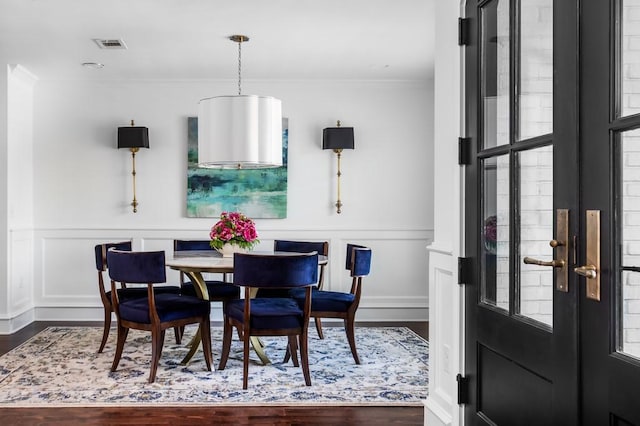 dining room featuring visible vents, a wainscoted wall, ornamental molding, wood finished floors, and a decorative wall