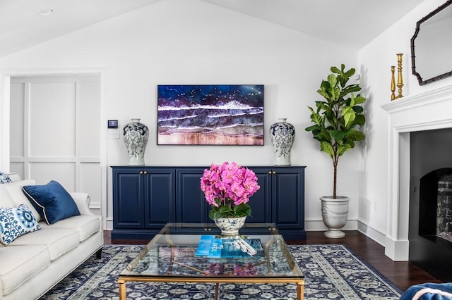 living area featuring dark wood finished floors, lofted ceiling, a fireplace, and baseboards