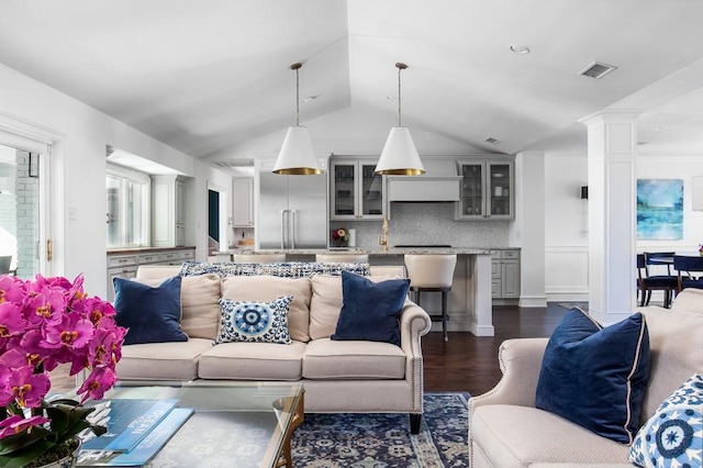 living area with vaulted ceiling, dark wood-style floors, visible vents, and ornate columns