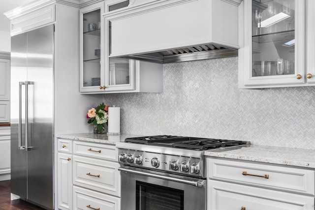 kitchen with custom exhaust hood, premium appliances, tasteful backsplash, and light stone countertops