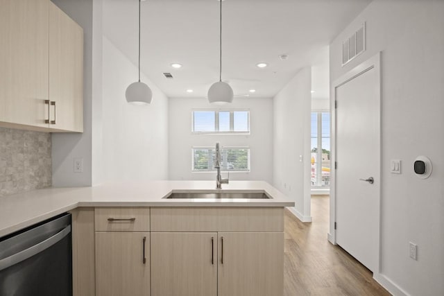 kitchen featuring light brown cabinets, visible vents, a peninsula, a sink, and stainless steel dishwasher