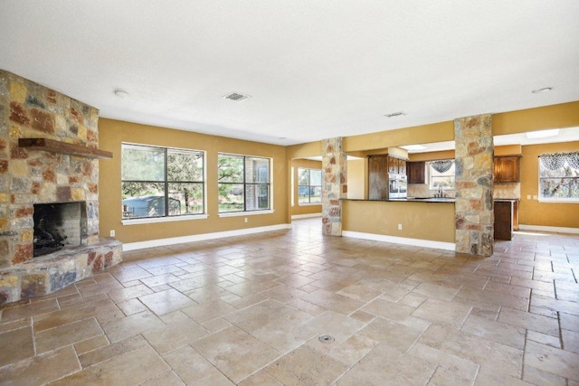 unfurnished living room featuring a stone fireplace, baseboards, visible vents, and stone tile flooring