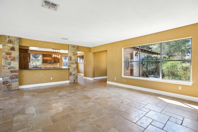 unfurnished living room with visible vents, baseboards, and stone tile flooring